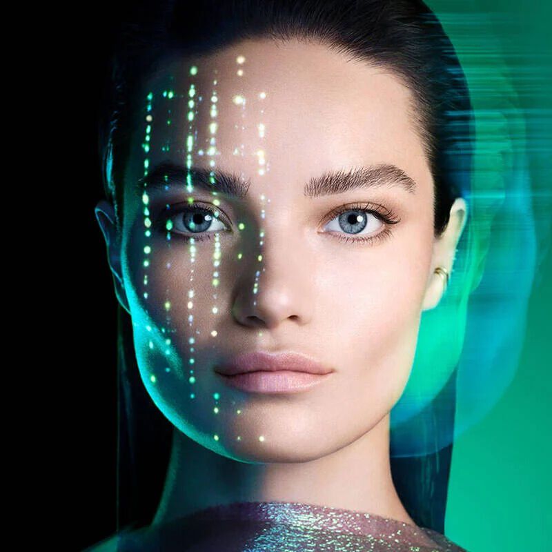 une femme aux cheveux fonces et aux yeux bleus, le regard droit devant elle sur un fond vert