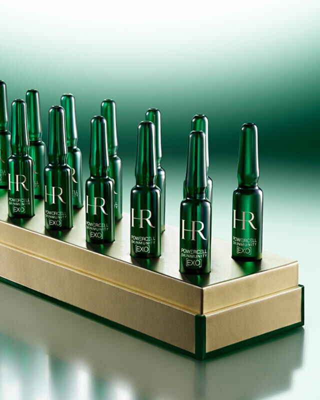 14 ampoules monodoses Powercell Skinmunity EXO vertes, presentees sur un socle dore de luxe.
