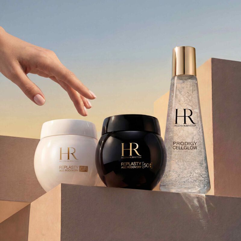 Helena Rubinstein Prodigy Cellglow serumfles (helder, bubbels) en Re-Plasty cremepot (zwart). Geplaatst op een getextureerde en lichtgevende witte achtergrond, wat elegantie en huidverzorgingseffectiviteit symboliseert.