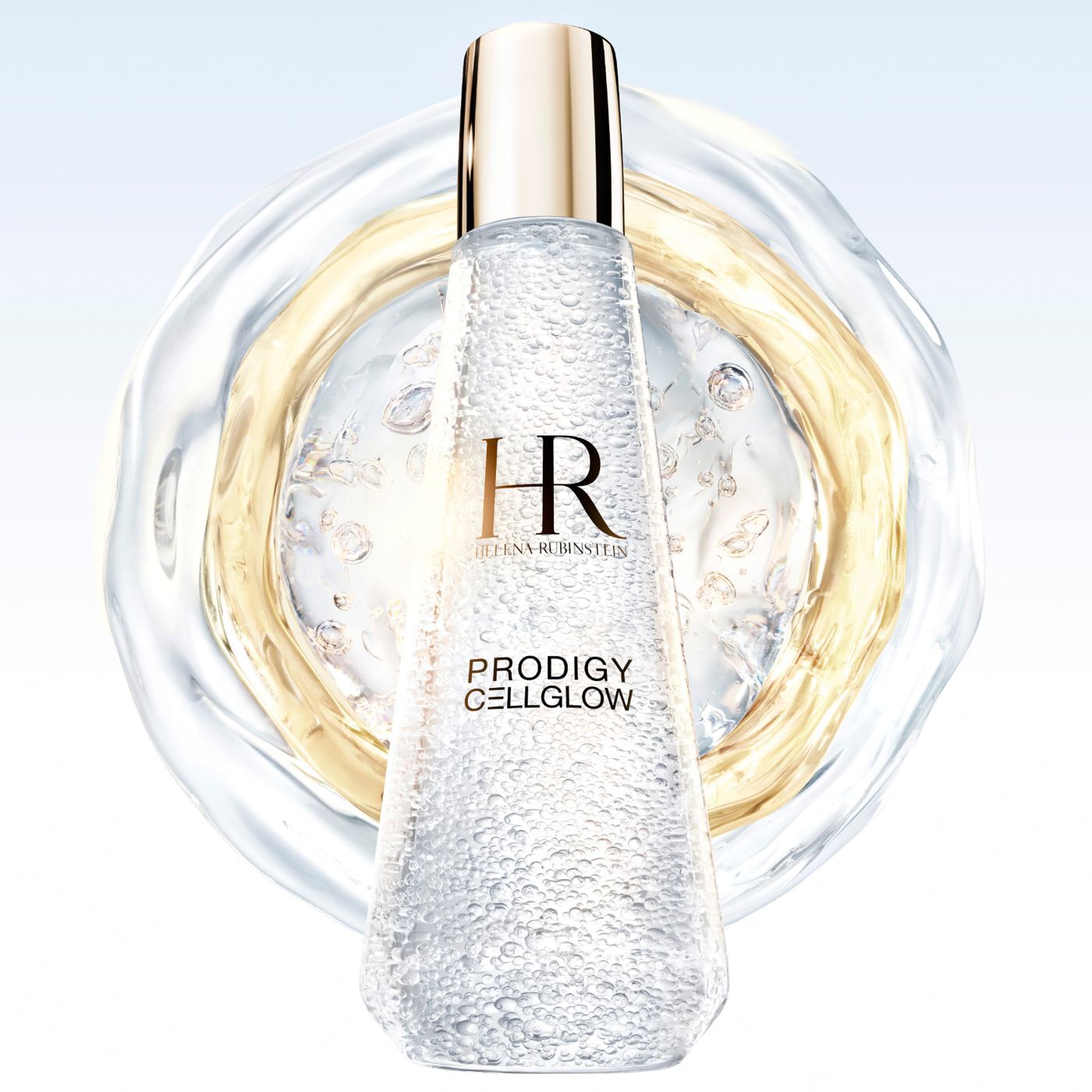 "Helena Rubinstein Prodigy Cellglow" serumfles gevuld met belletjes, in het midden van doorschijnende en gouden vloeibare ringen die zich uitstrekken over een lichte achtergrond.